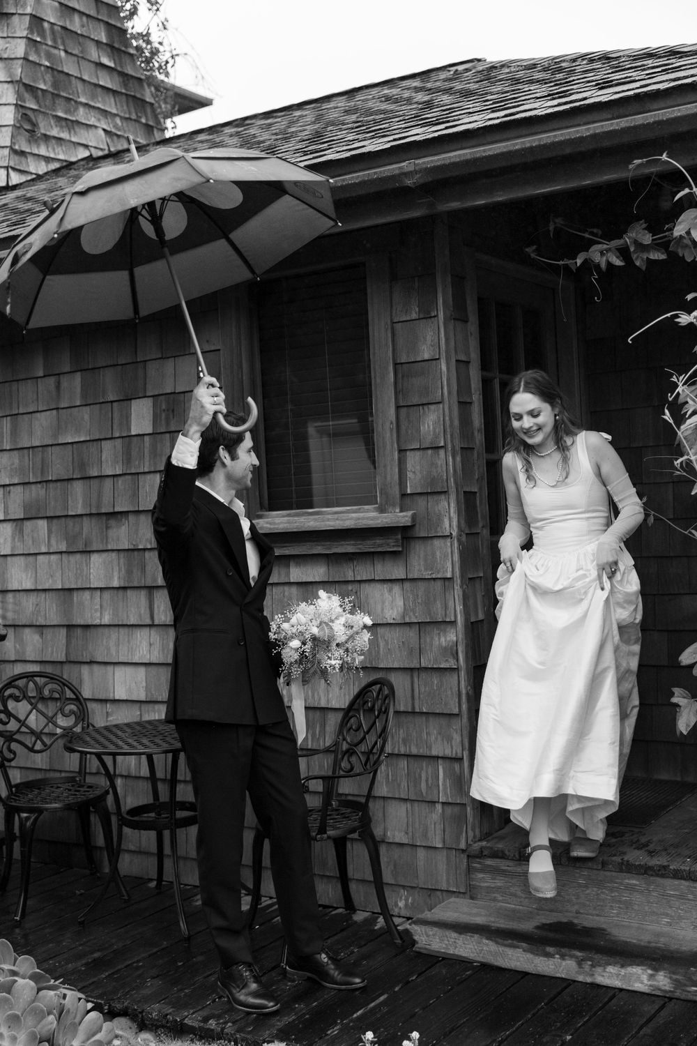 Wedding couple shares playful moments under umbrellas on a rustic cabin porch.