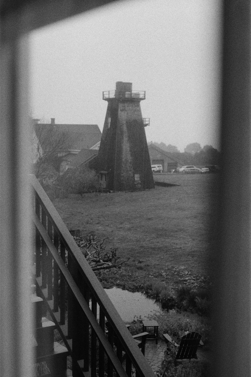 A black and white photograph of an old wooden lighthouse tower and buildings on a misty coastline.