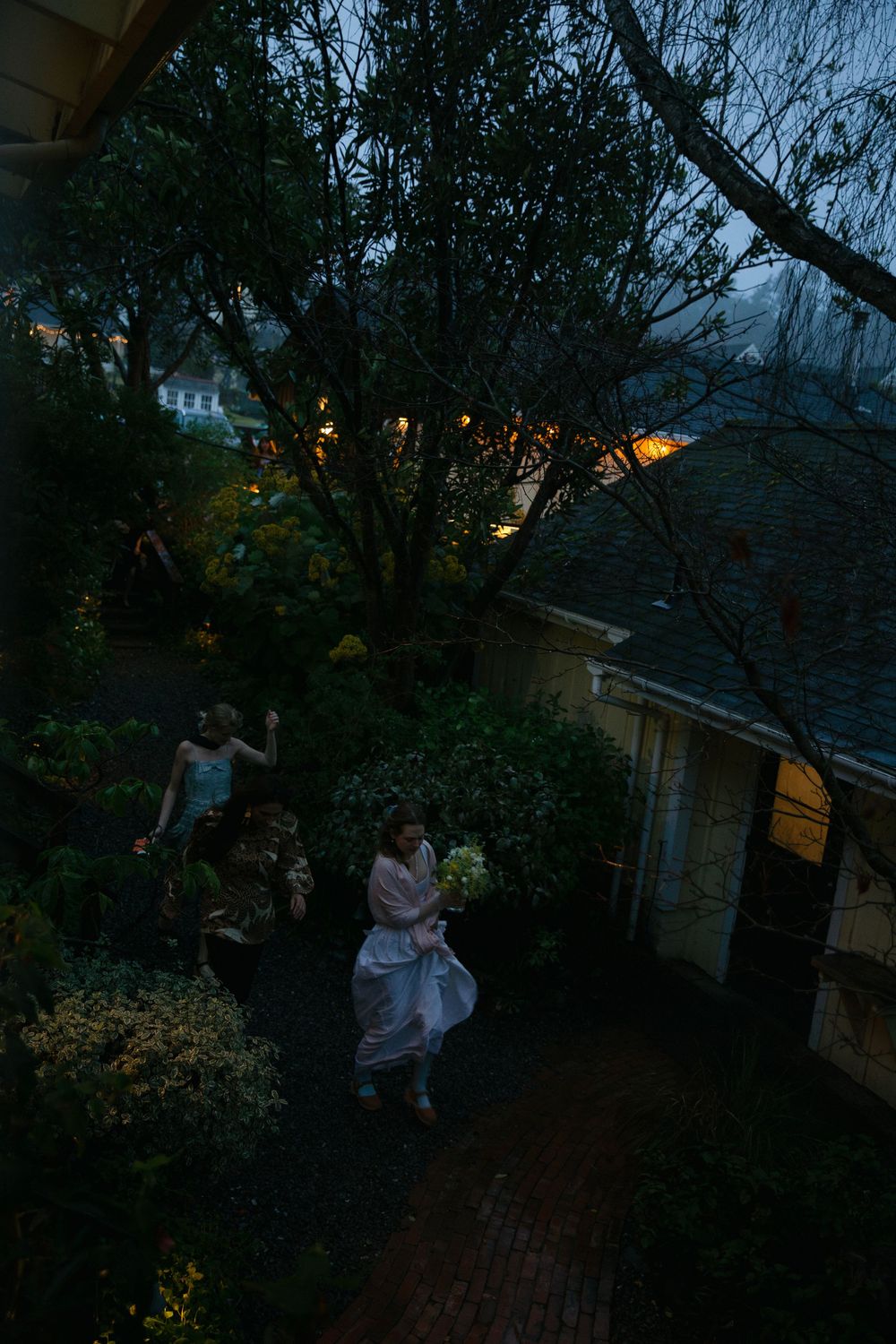 Evening garden scene with figures walking among trees and houses.