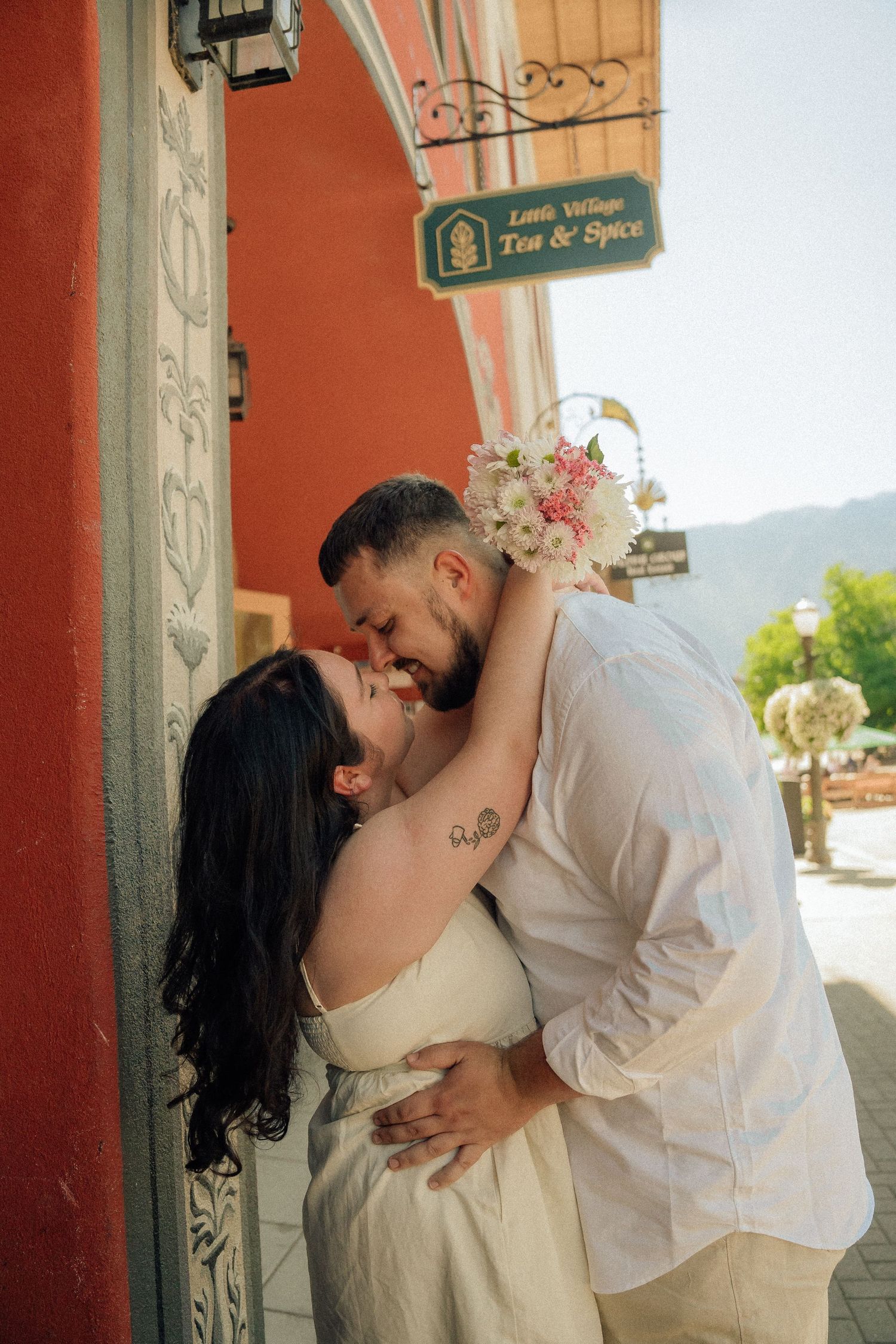 A romantic couple embraces and shares a tender moment against a coral-colored wall with scenic mountains in the background.