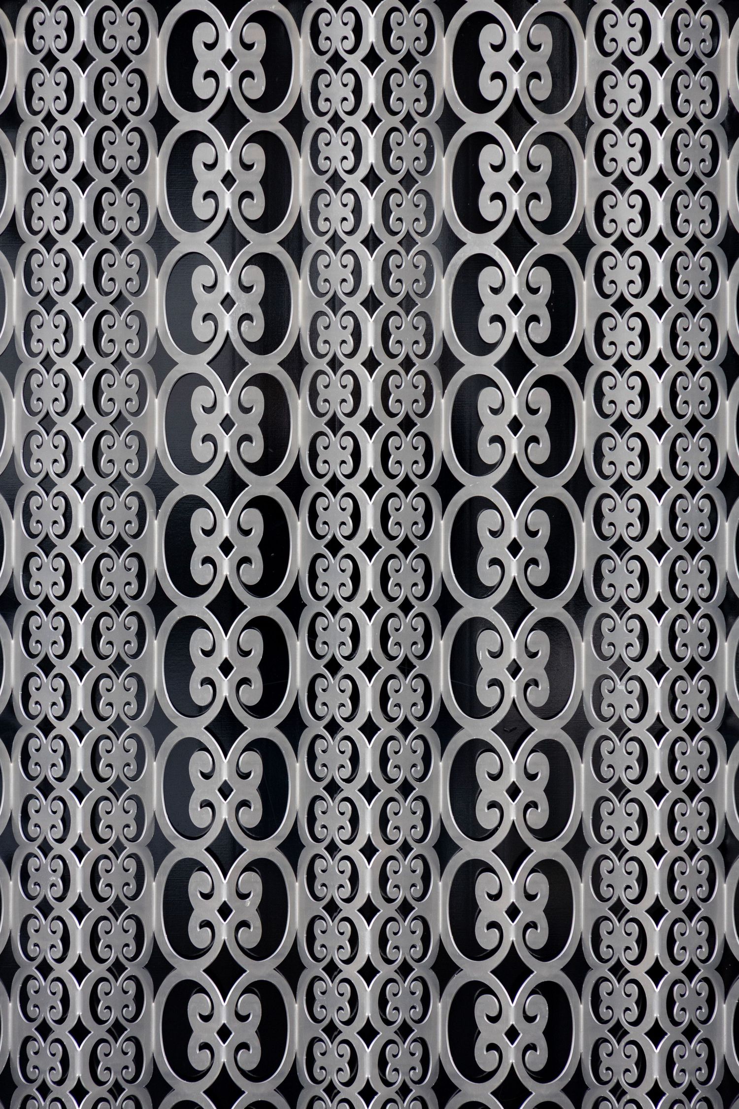 Close-up of a decorative metal screen with a repeating geometric pattern of interlocking circles and ovals in vertical rows.