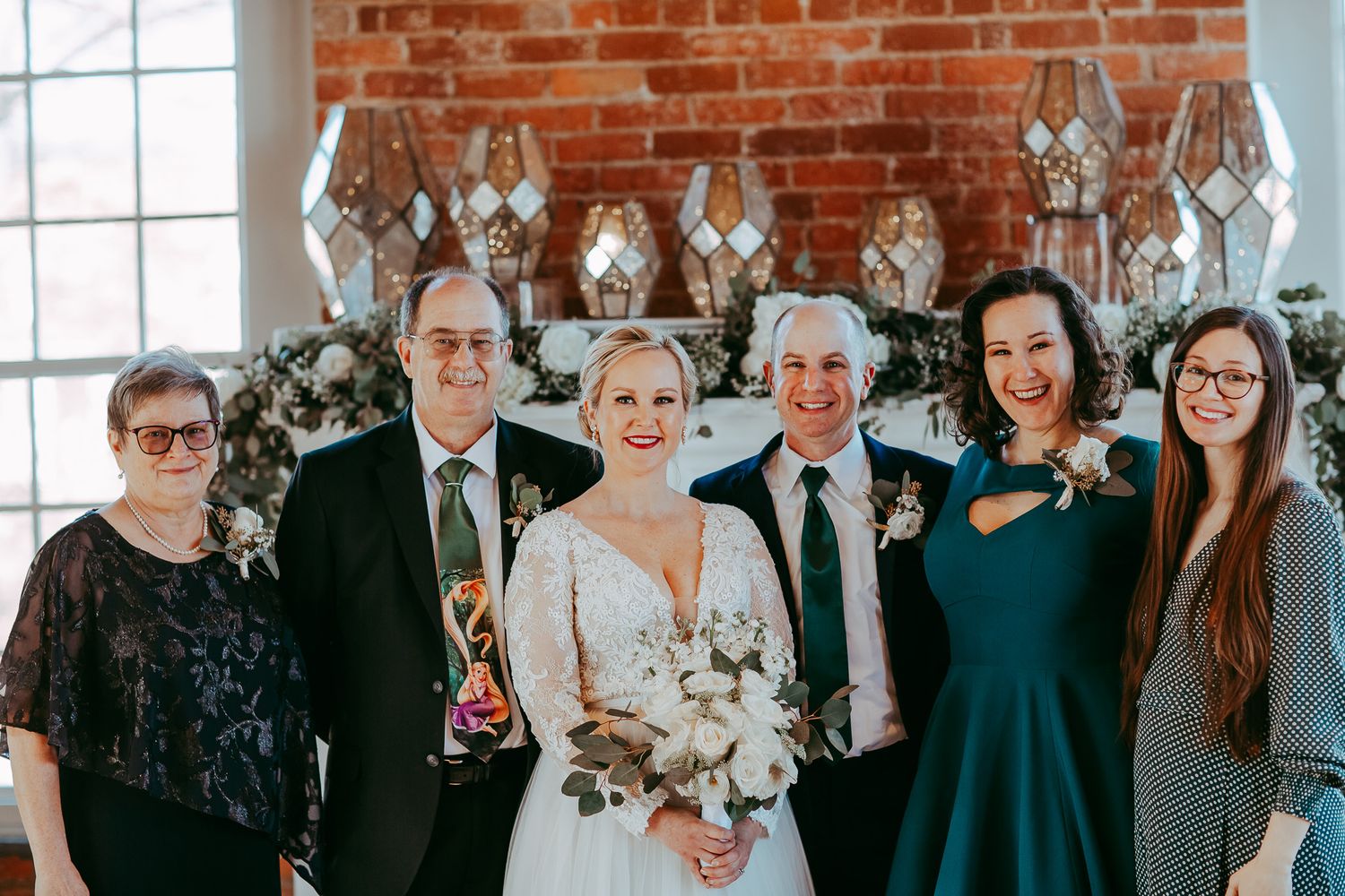 Wedding party portrait with vintage brick backdrop and hanging geometric decorations.