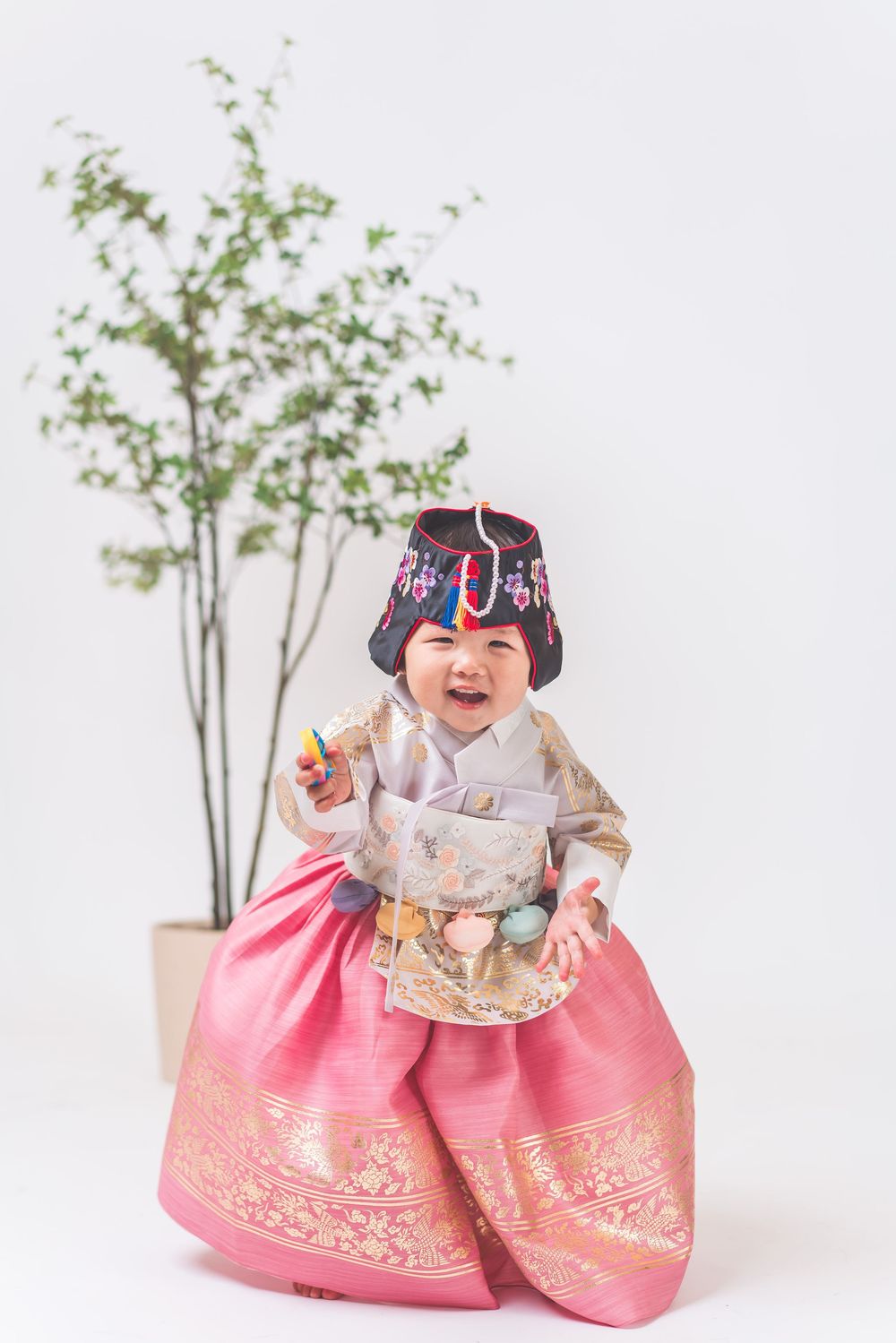 Joyful moment in traditional Korean hanbok dress next to potted plant.