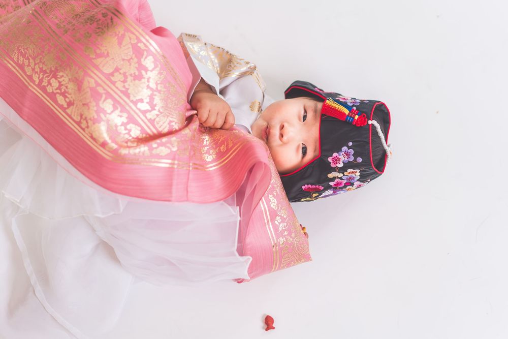 Elegant pose in pink and gold traditional Korean hanbok against white background.