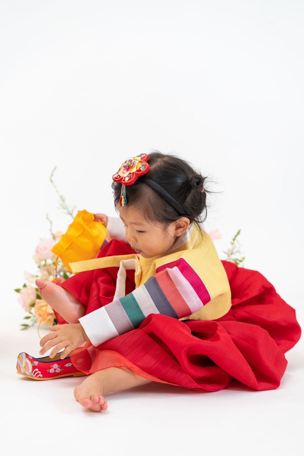 Child in red hanbok dress exploring traditional Korean items and clothing.
