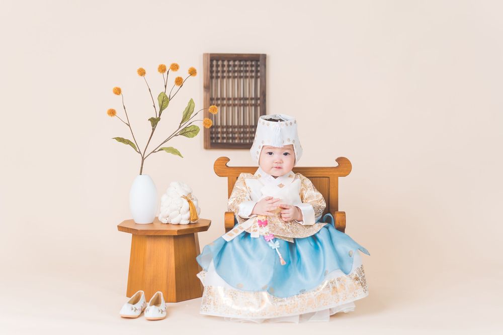 Child in vintage-style dress sitting at wooden table with decorative floral arrangement.