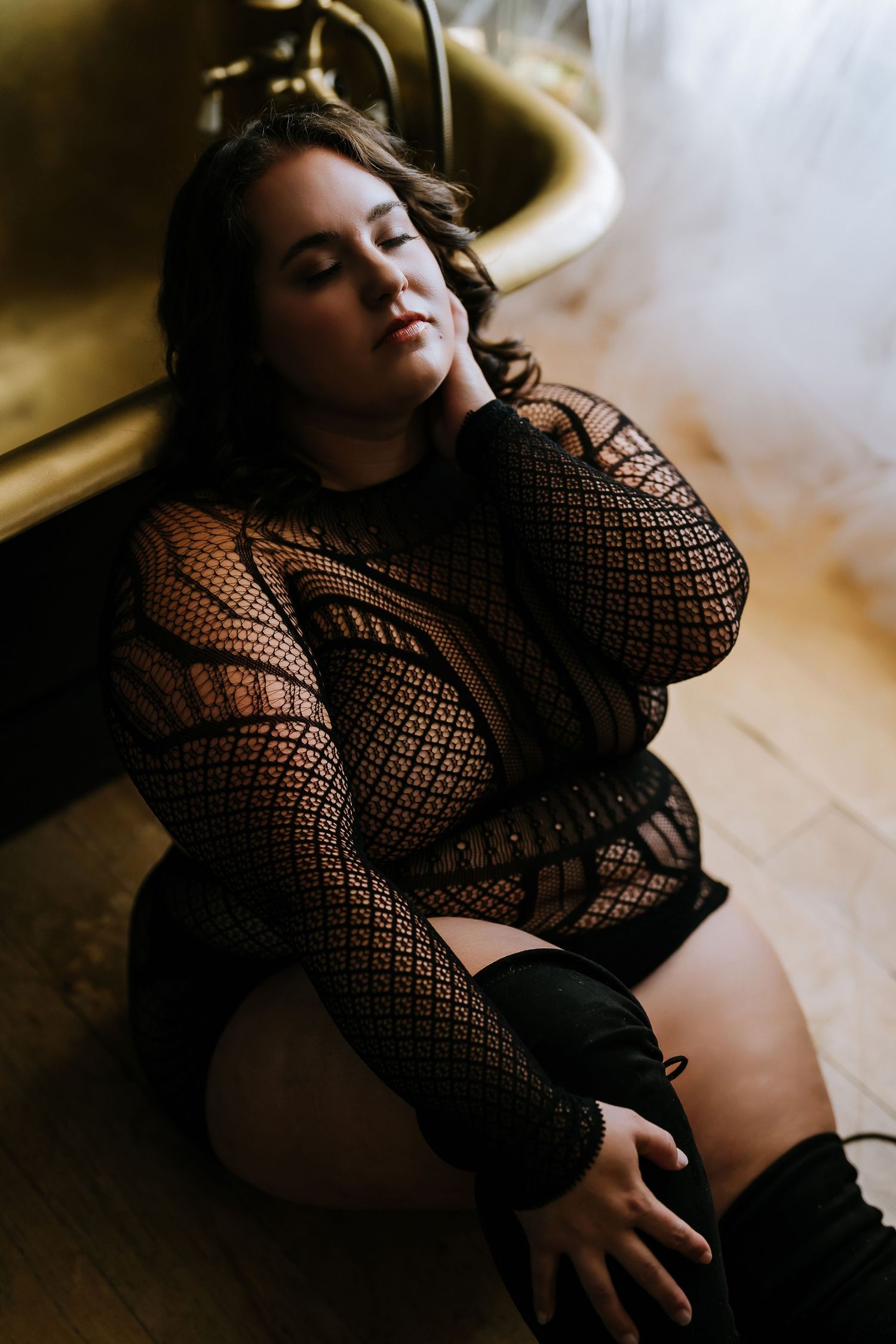 Artistic boudoir photography featuring a black lace bodysuit in moody lighting with dramatic shadows.