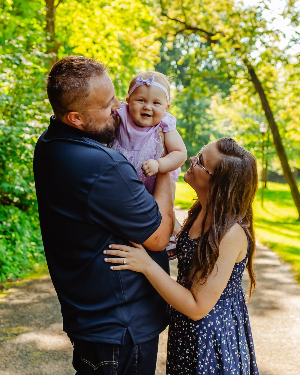 Young family enjoying a tender moment together on a sunny day in a park with lush green trees in the background.