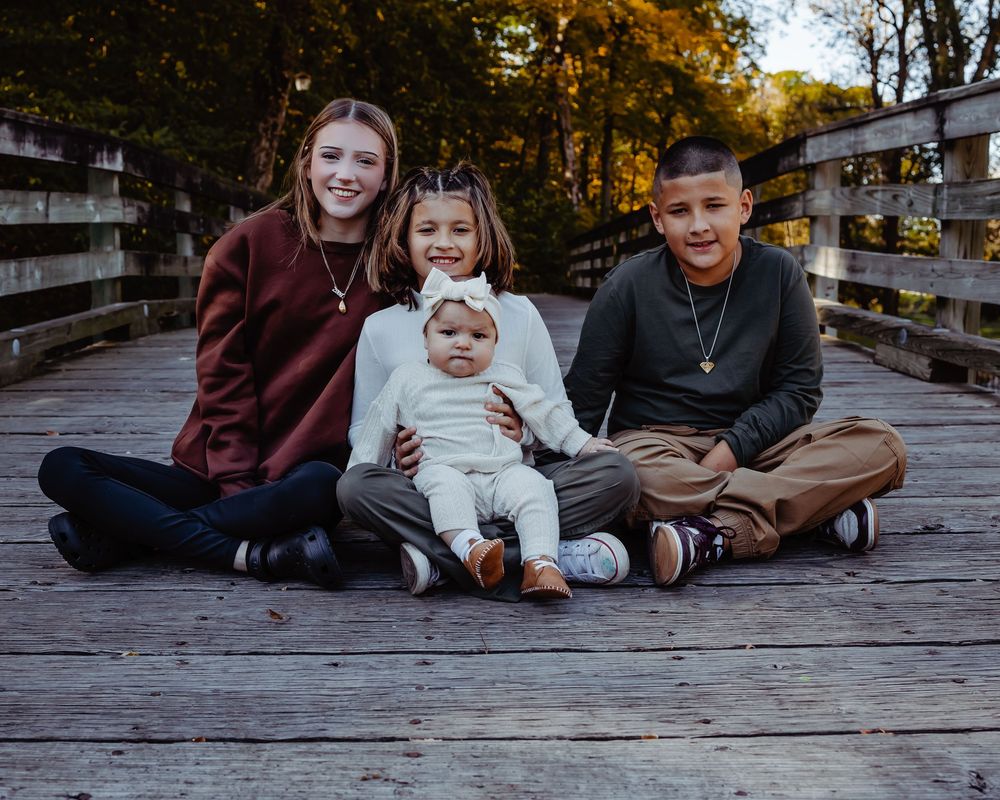 A family sits together on a wooden deck during autumn with golden trees in the background.