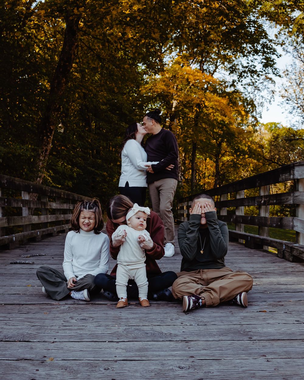 A group sits together on a wooden bridge in autumn with golden foliage in the background.