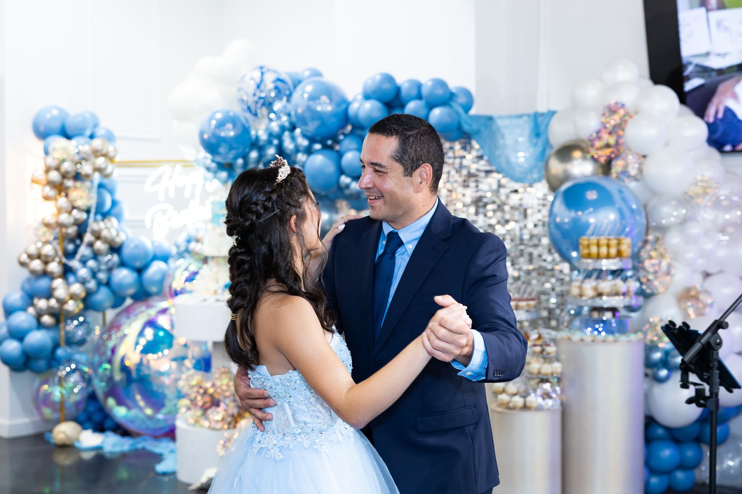Couple dancing at celebration with elaborate blue and gold balloon arch decorations.