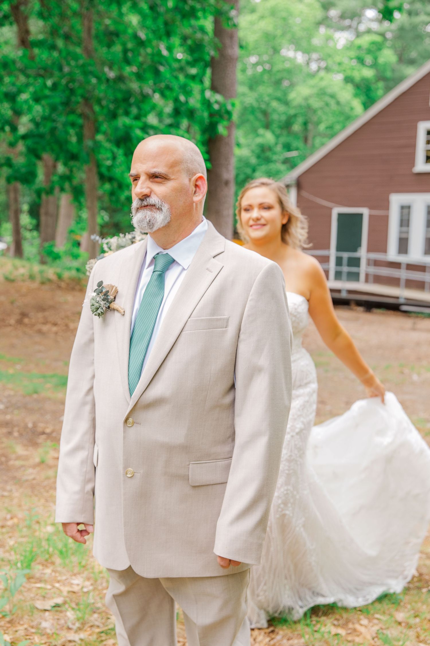 A joyful outdoor wedding moment at a rustic venue with lush green trees and a brown wooden cabin in the background.