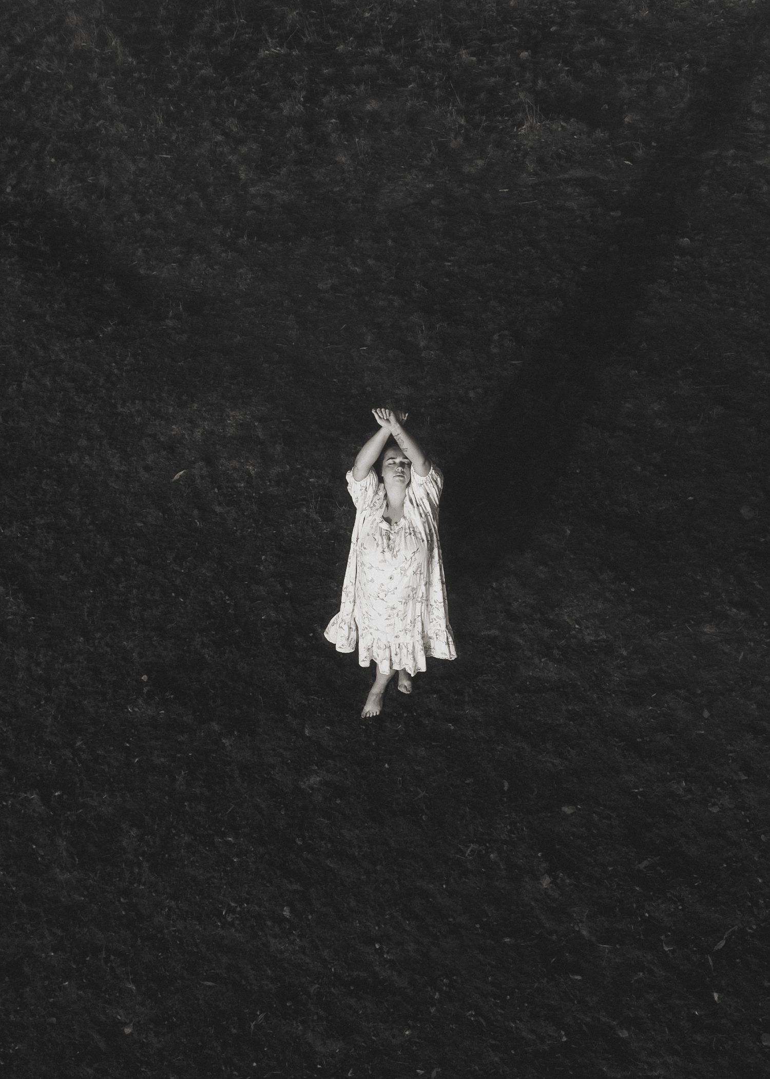 A solitary figure in a white dress appears to be floating or suspended against a stark black background in this artistic image.