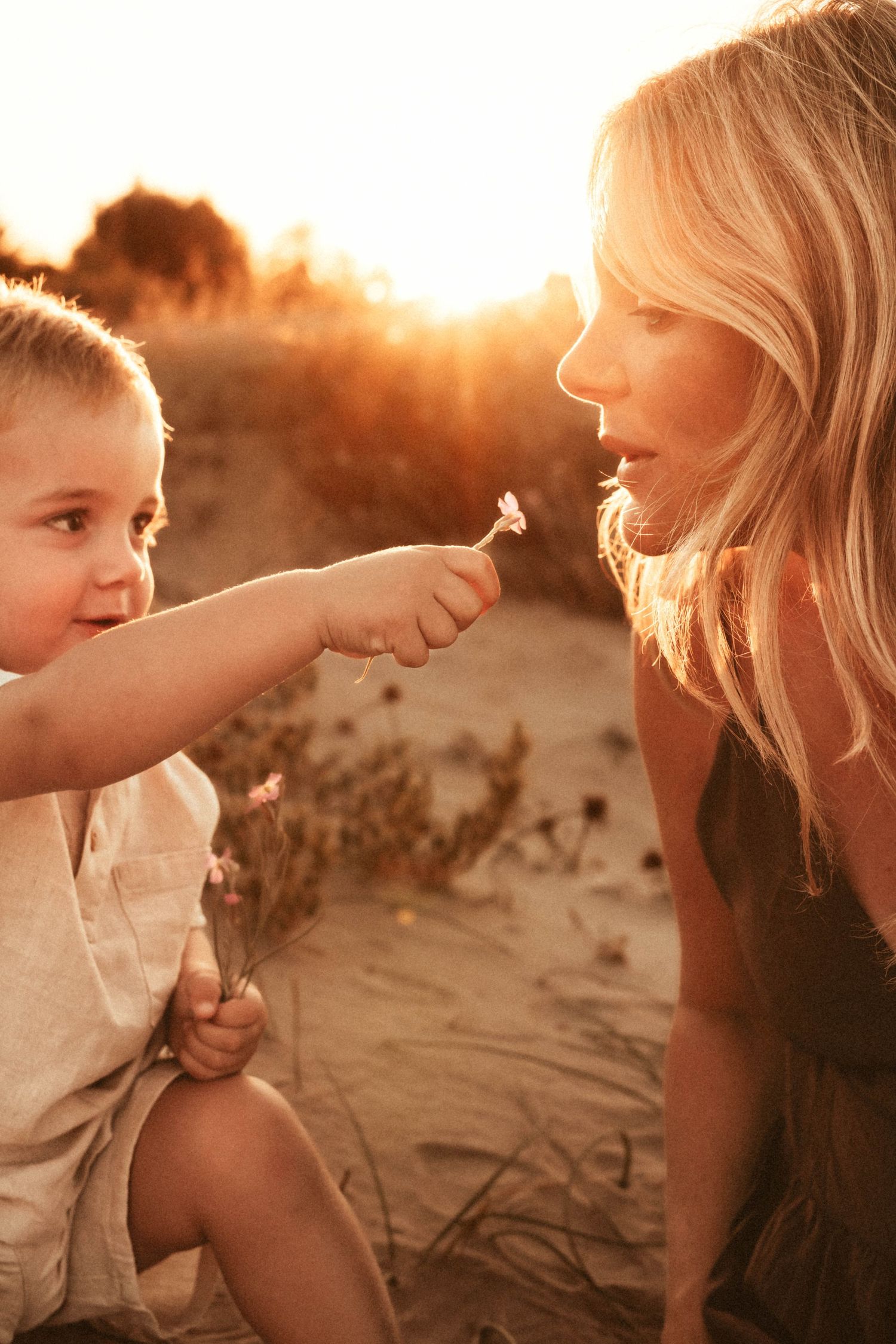 A sweet moment captured at sunset on the beach as a child shares a flower with someone in warm golden light in Javea, family photographer