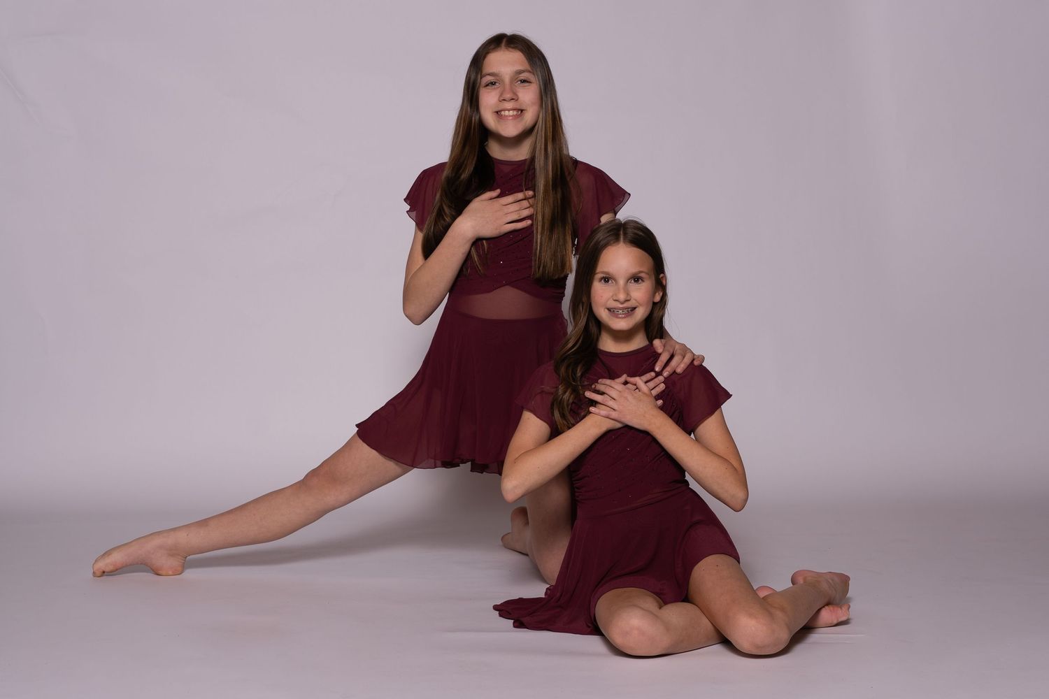 A group of dancers in burgundy dresses pose together for a dance team photo shoot against a light gray backdrop.