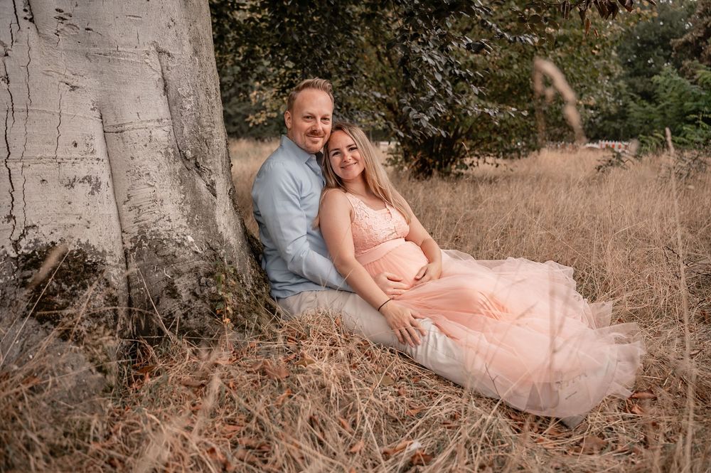A couple in formal attire poses together on dried grass during an outdoor photo session.