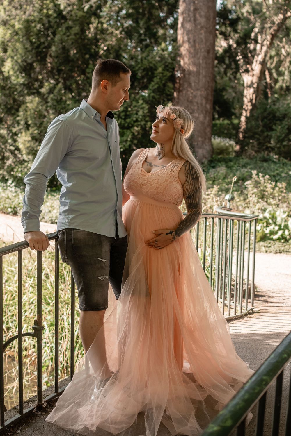 A couple shares a tender moment on a bridge during their maternity photoshoot.