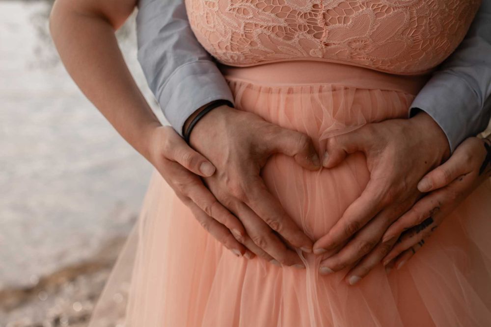 Hands forming a heart shape over a peach-colored tulle dress in an intimate maternity photo.