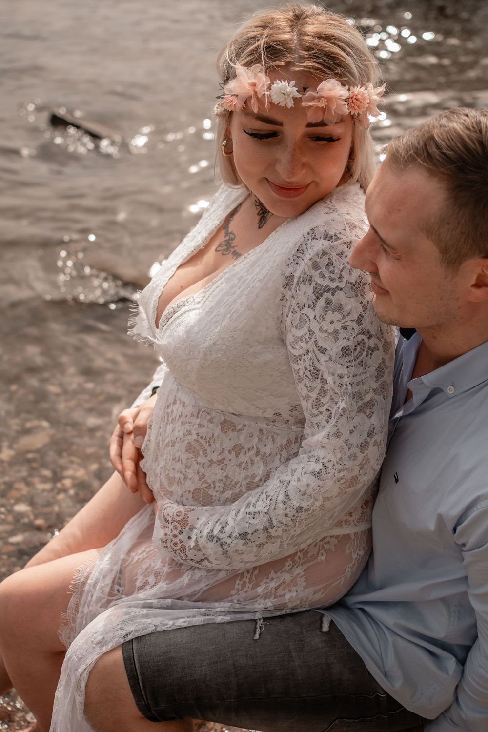 A romantic maternity photo by the water featuring a couple in elegant attire.
