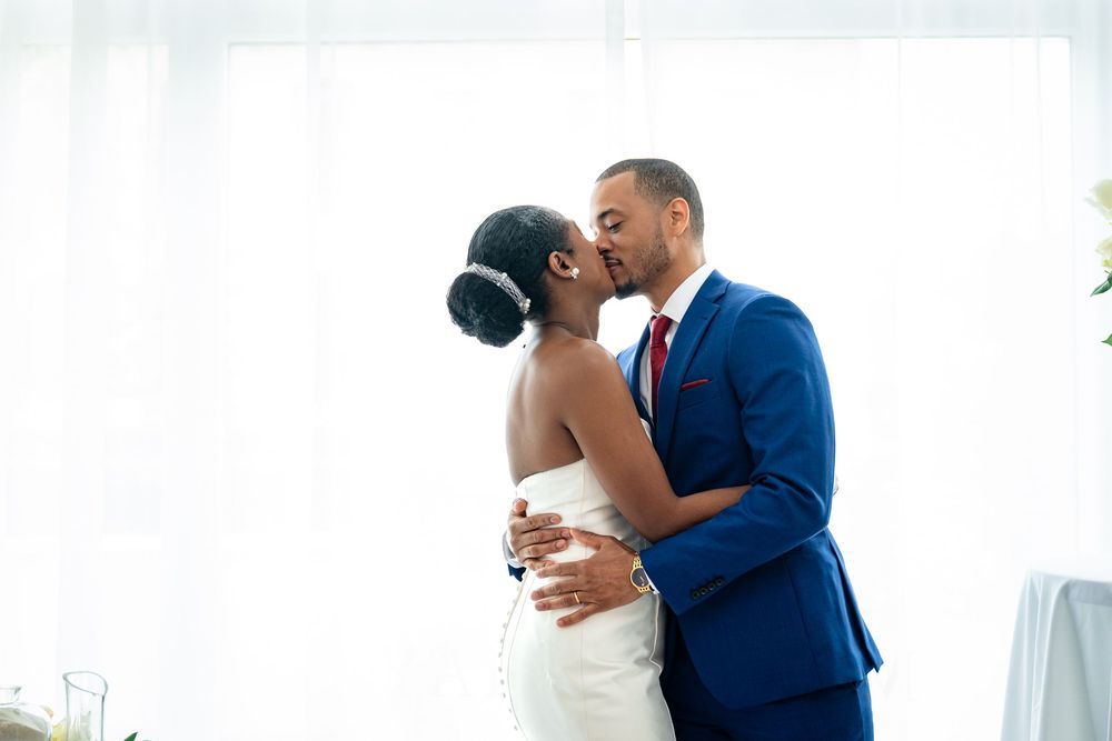 A romantic couple in wedding attire embrace tenderly by a window in an intimate moment.