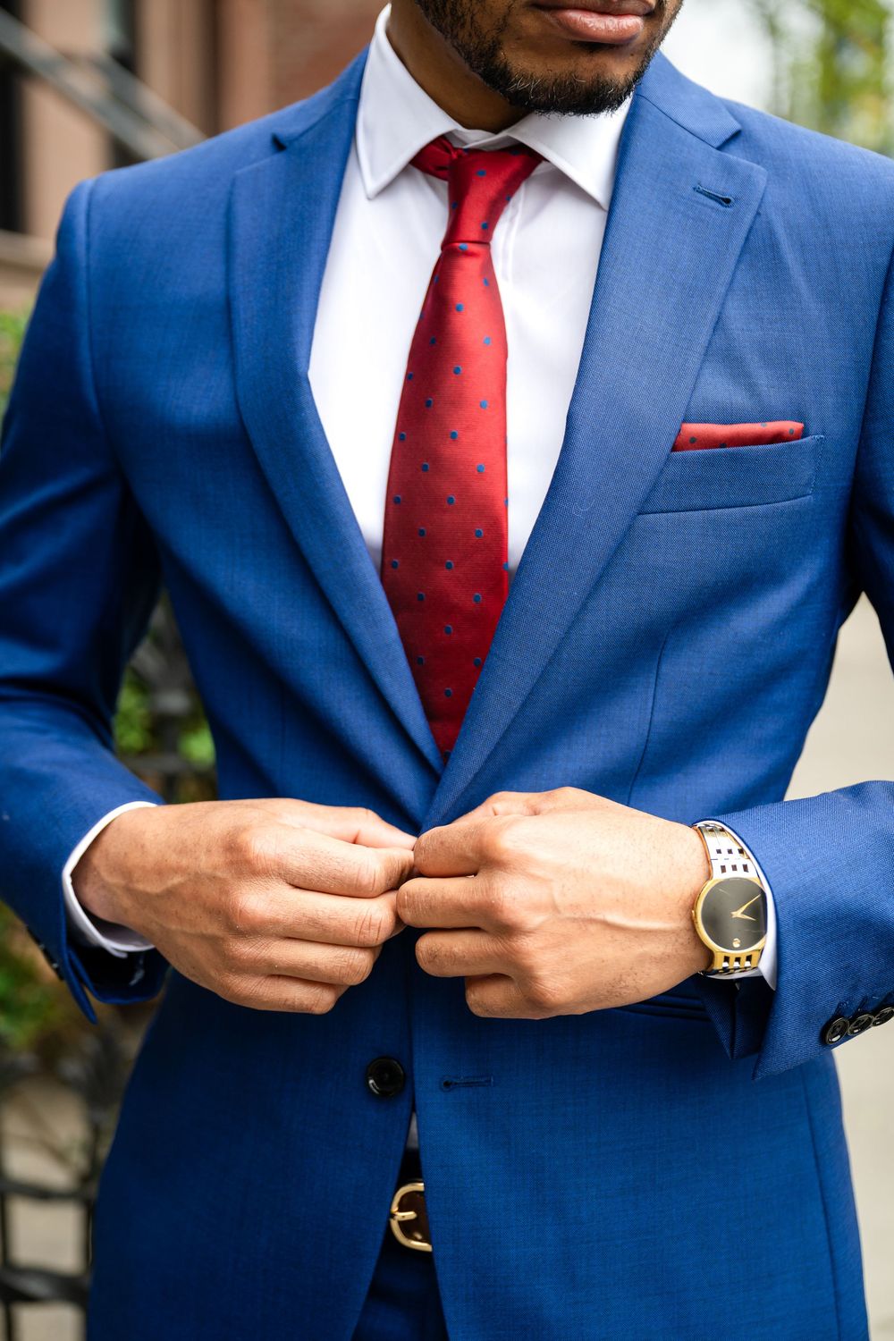 Close-up of royal blue suit jacket with red polka dot tie and silver watch, showing professional business attire details.