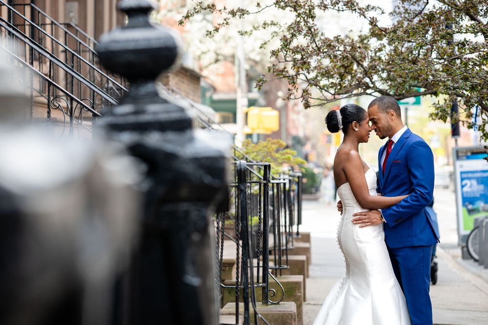 A couple in wedding attire pose for photos on an urban sidewalk.