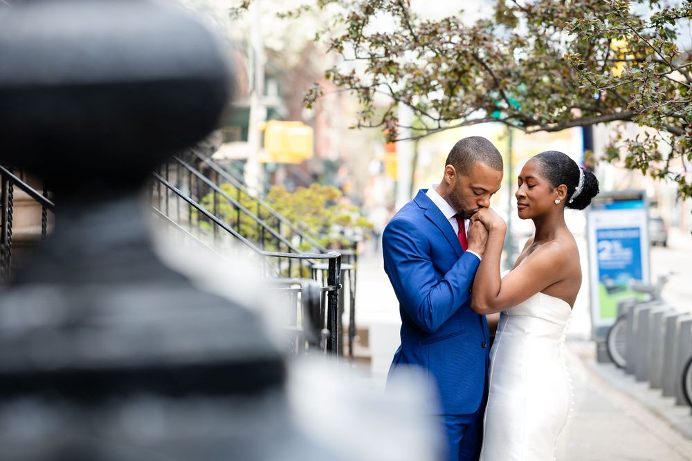 A couple sharing an intimate moment outdoors, with a person in a navy blue suit and white wedding dress.