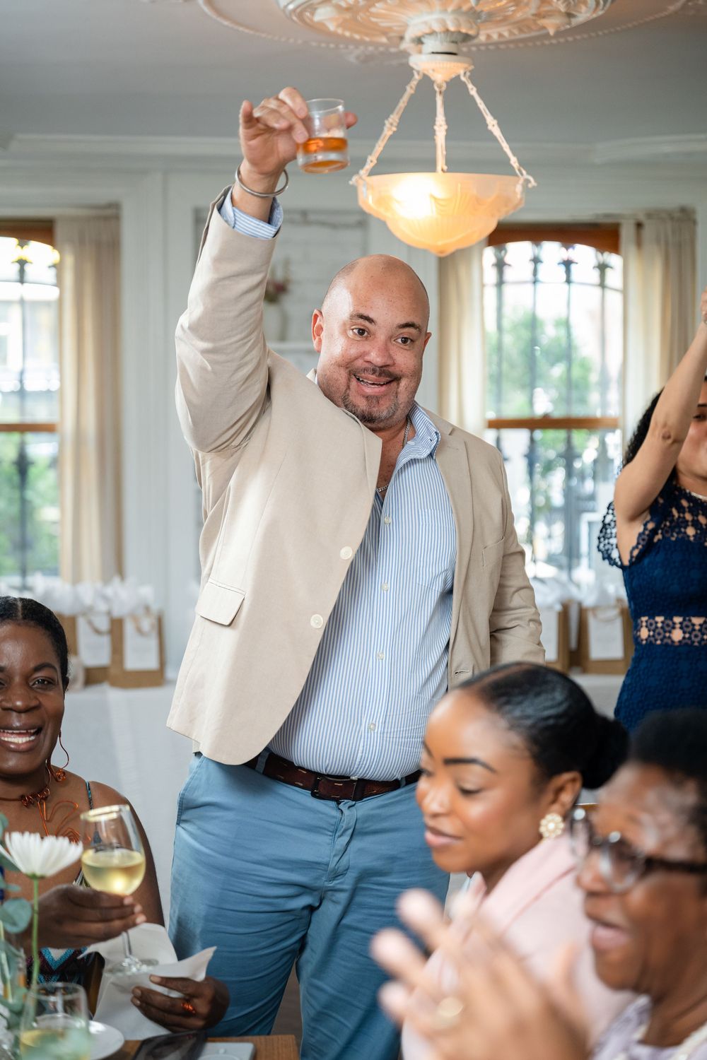 A celebratory gathering in an elegant dining room with chandelier lighting as someone makes a toast with drinks.
