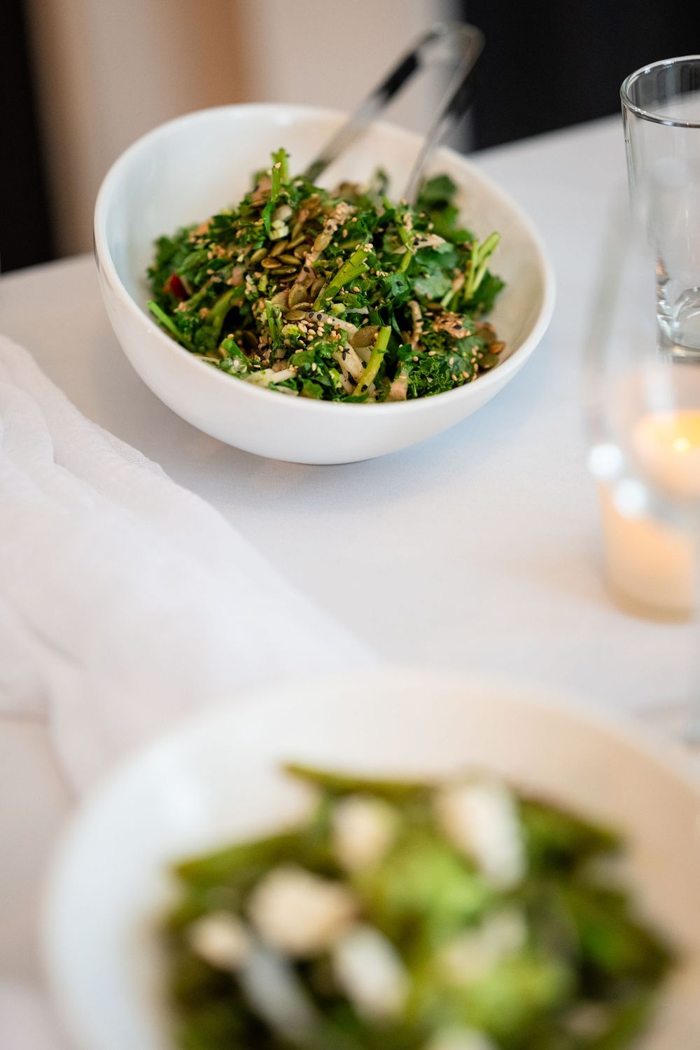 Fresh green salad topped with sesame seeds served in a white bowl on an elegant table setting.