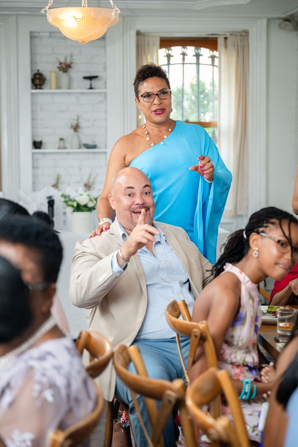 Lively celebration at an indoor dinner party with guests enjoying themselves under an ornate chandelier.