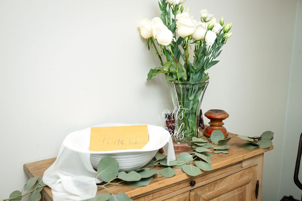 White roses in a glass vase with eucalyptus leaves on a wooden surface.