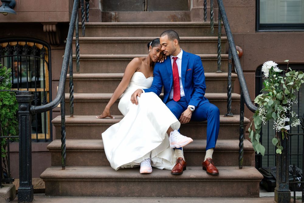 A newlywed couple sits together on brownstone steps in formal wedding attire.