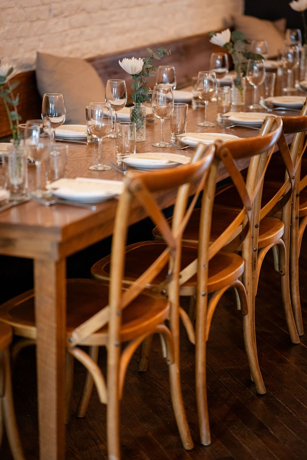 Elegant table setting with wooden crossback chairs and wine glasses in rustic dining room.