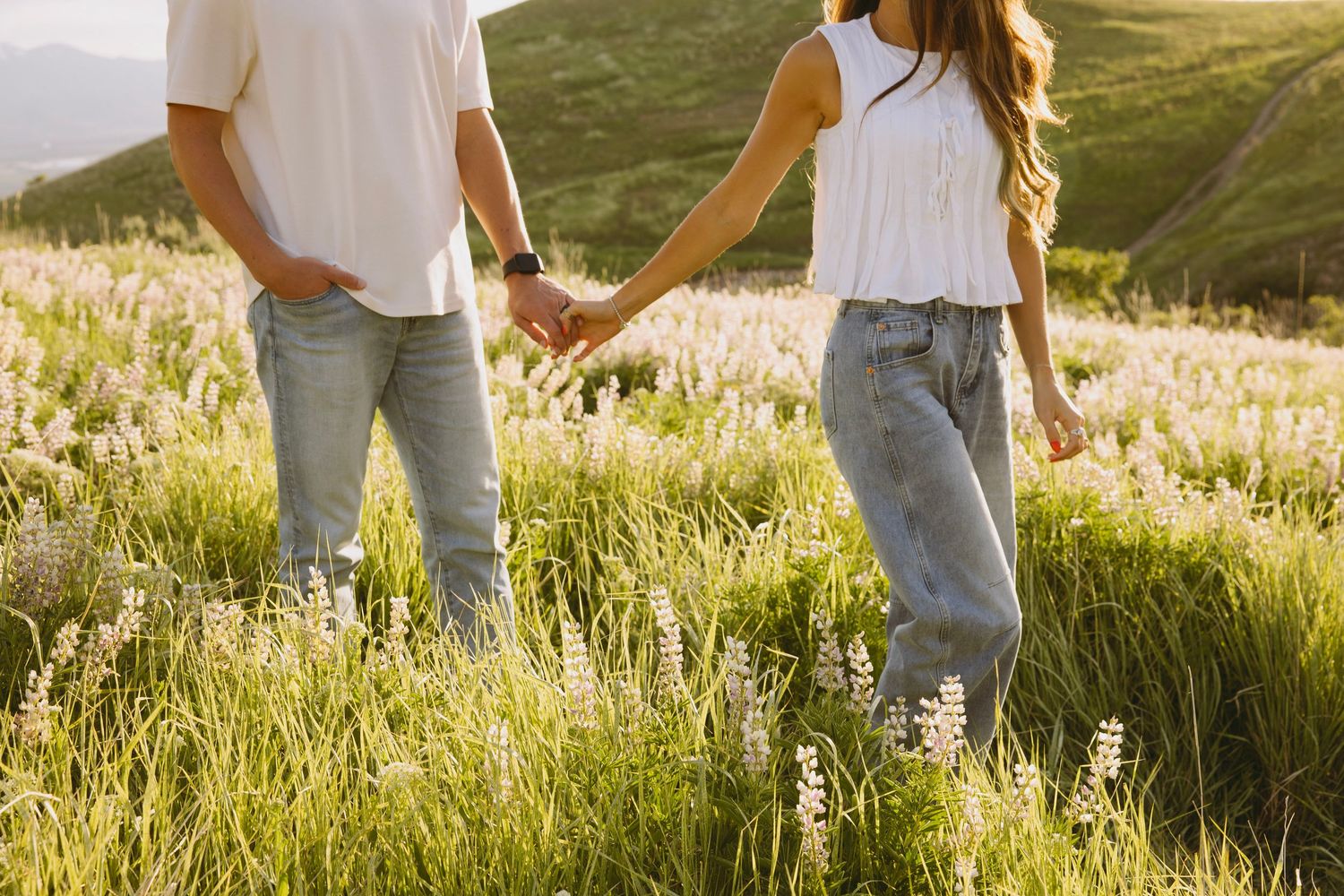 Romantic couple embraces near a mountain lake with snow-capped peaks in the background at sunset.