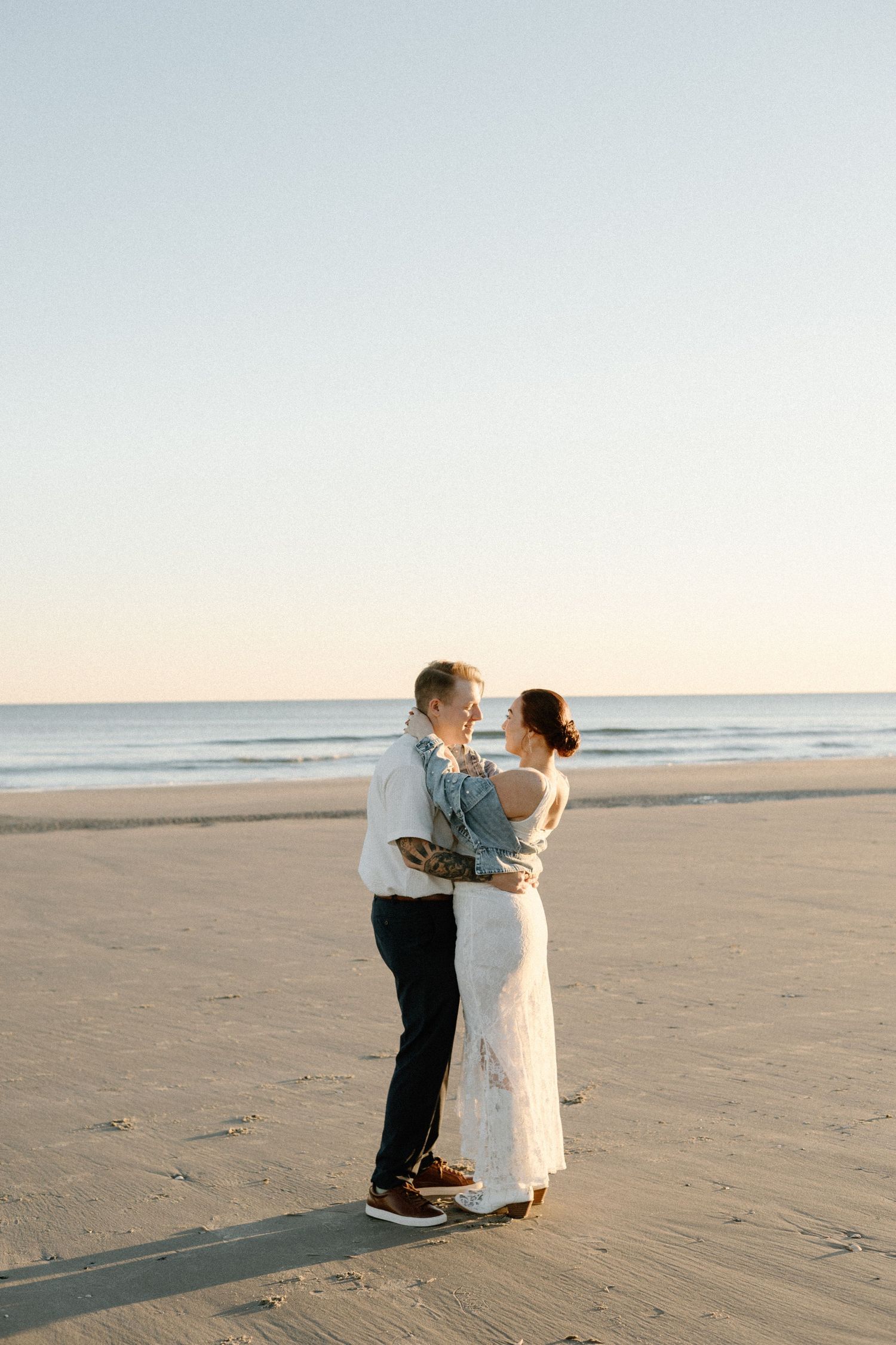 A romantic beach scene shows a couple standing together on a sandy shore at sunset.
