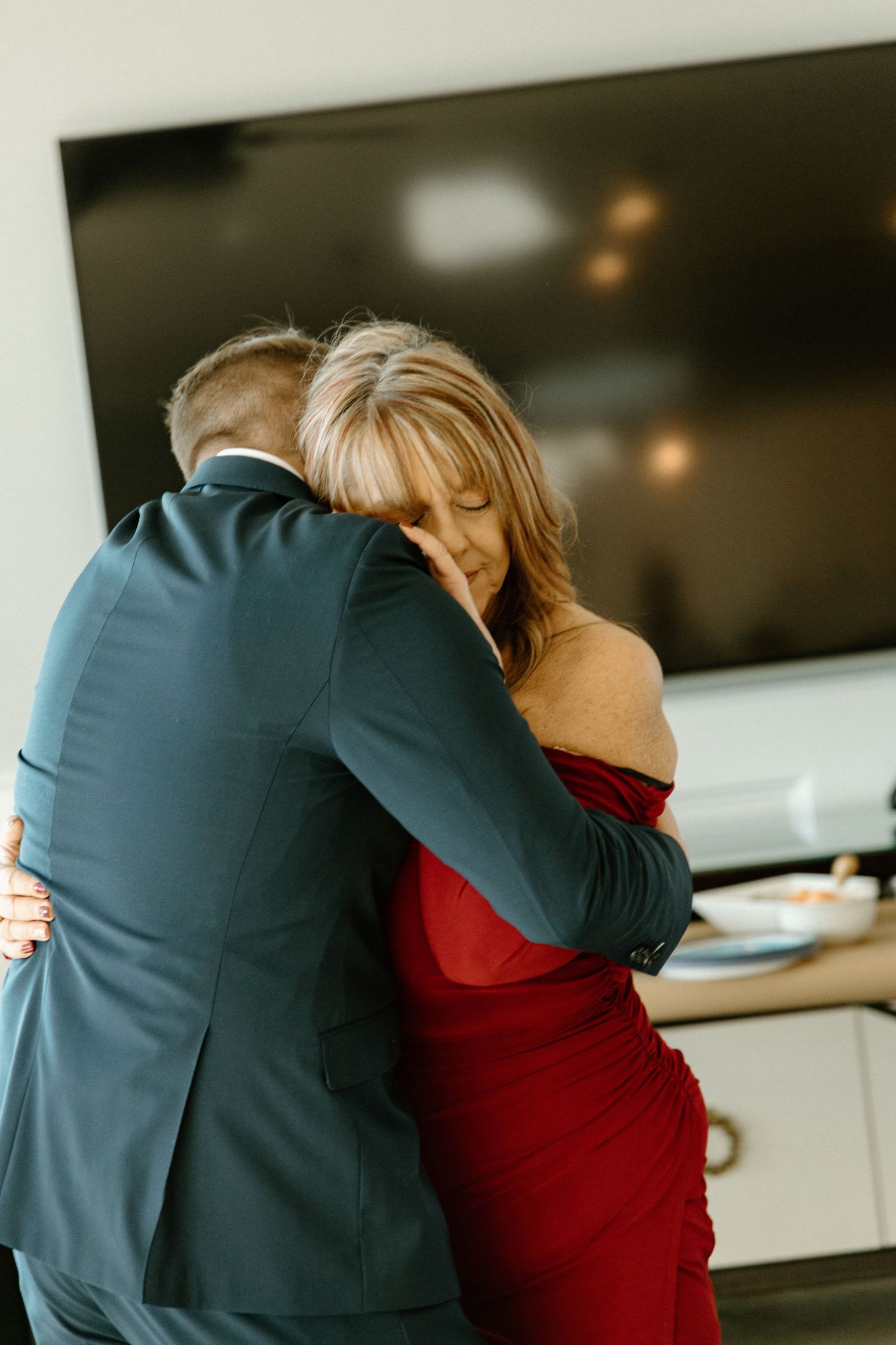 A couple shares an intimate dance, with the woman wearing a red dress and the man in a teal suit at an indoor event.