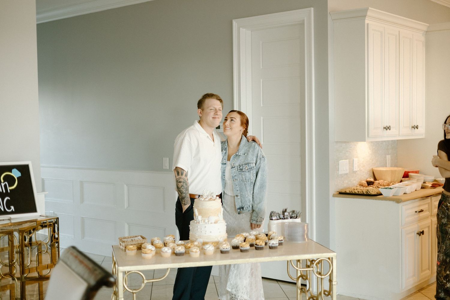 A couple shares an intimate moment in a bright kitchen while standing near a dessert table with baked goods.