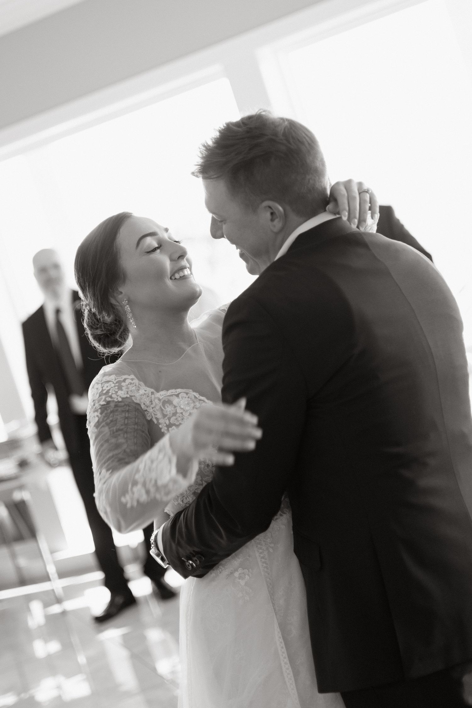 A joyful couple shares their first dance at a wedding reception in an elegant indoor venue, captured in black and white.