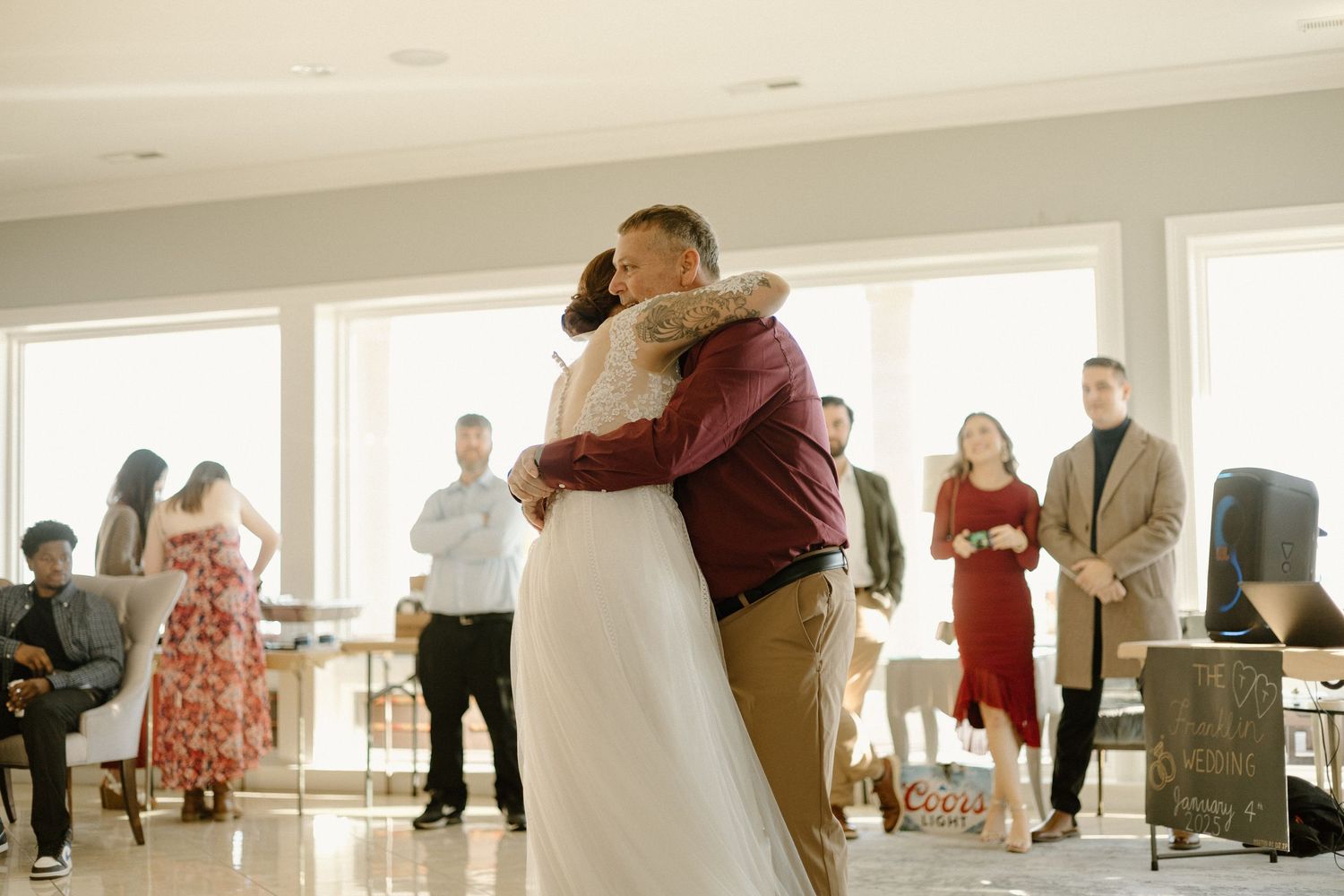 A couple shares their first dance as guests look on during a bright indoor wedding reception.