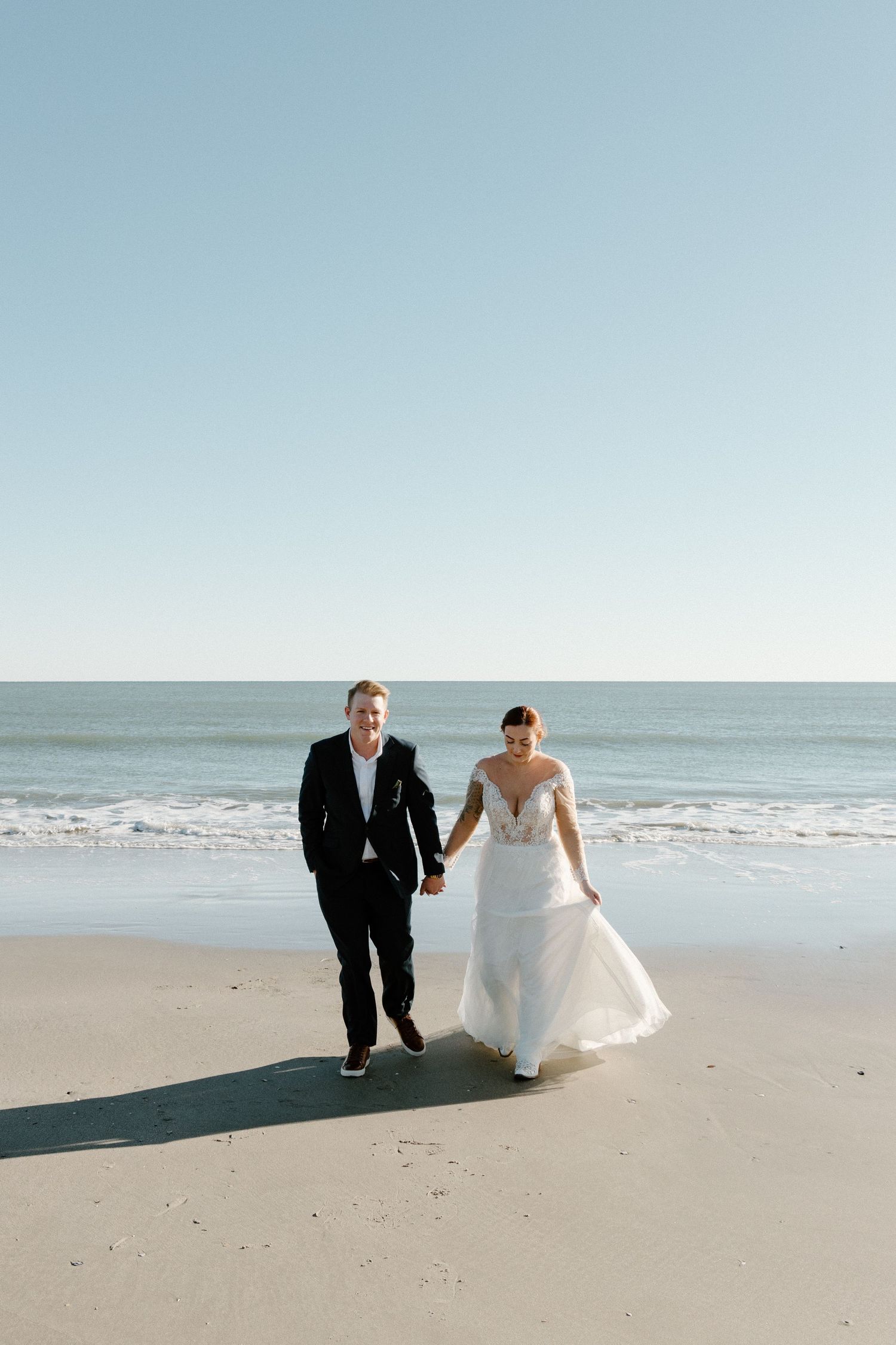Newlywed couple walking together on a serene beach with ocean waves in the background on their wedding day.