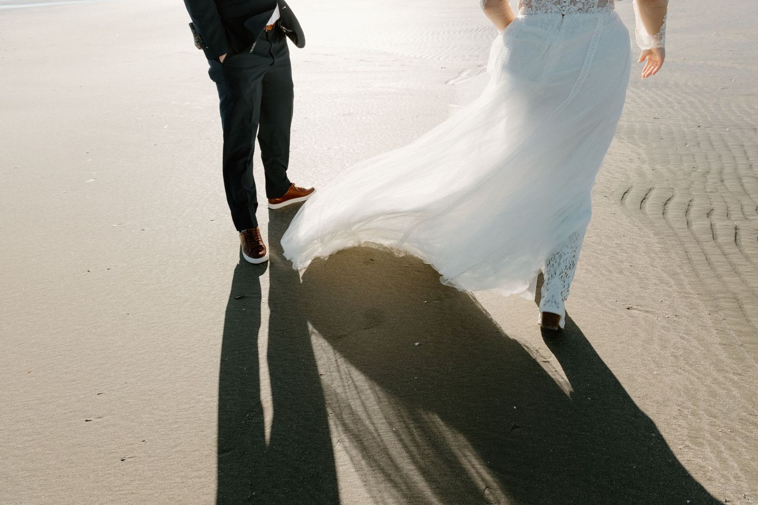 A couple holds hands on a cobblestone street as their shadows cast dramatic silhouettes in the sunlight.