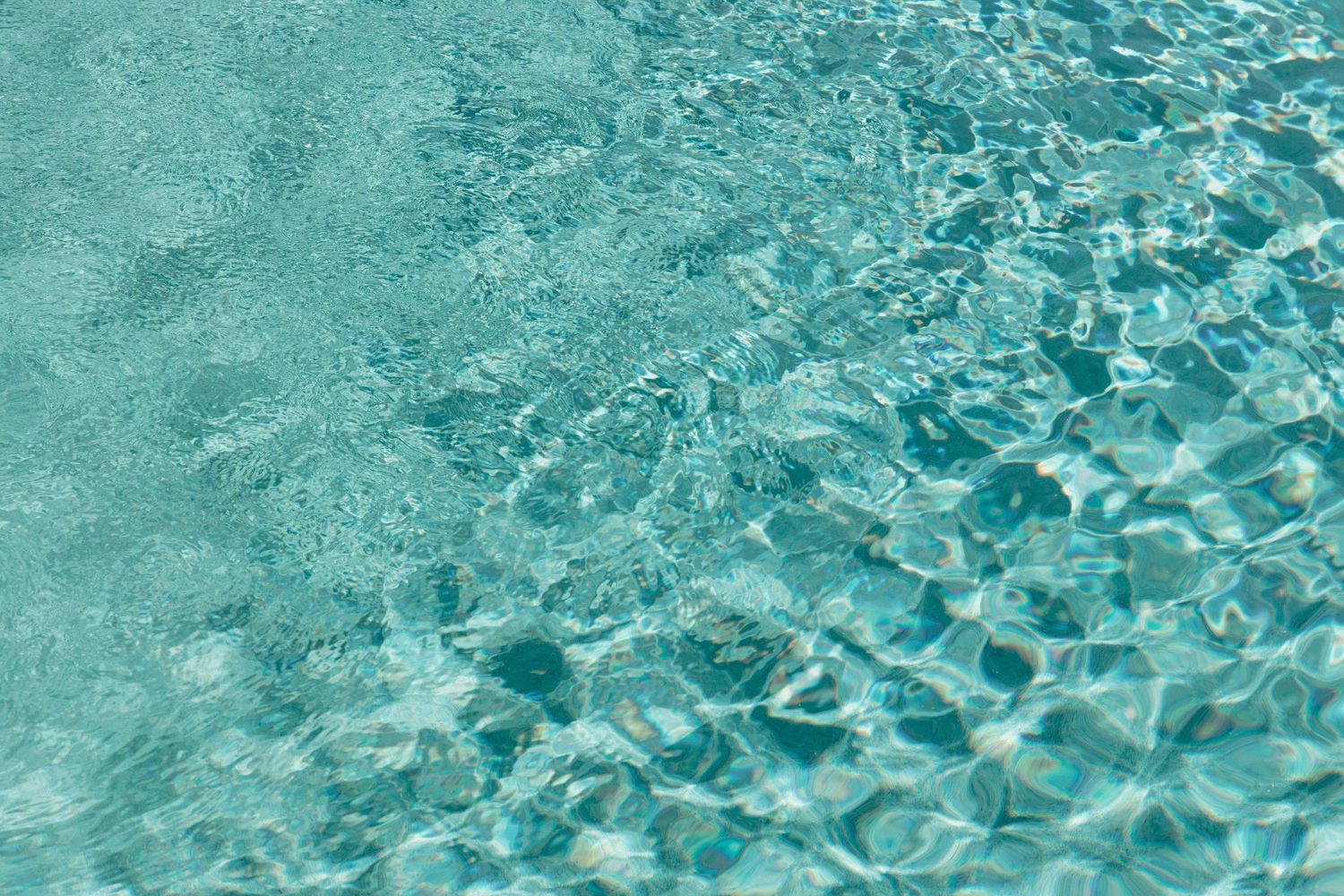 Crystal clear turquoise swimming pool water rippling with sunlight creating geometric patterns on the surface.