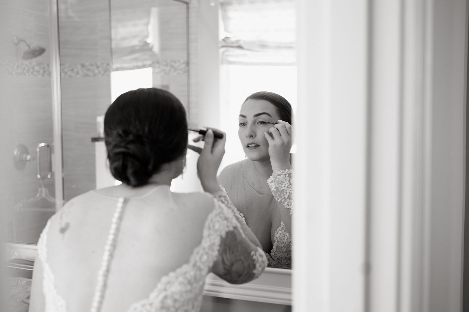 Person in lace dress looks into mirror while applying makeup for a formal event.