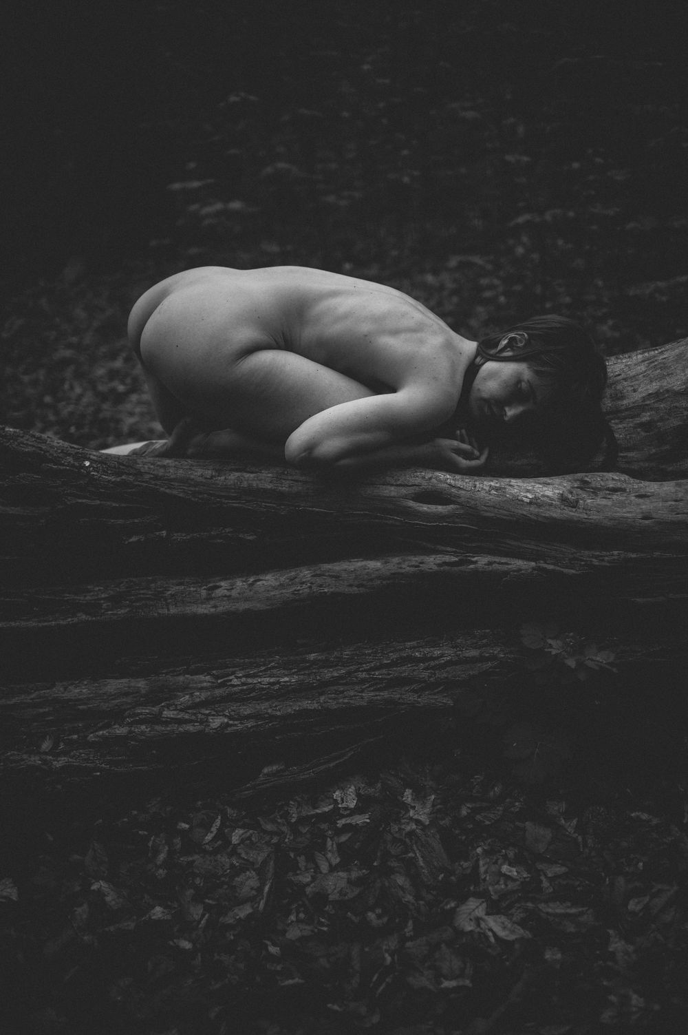 A artistic black and white nude figure study capturing peaceful repose against a dark rocky surface.