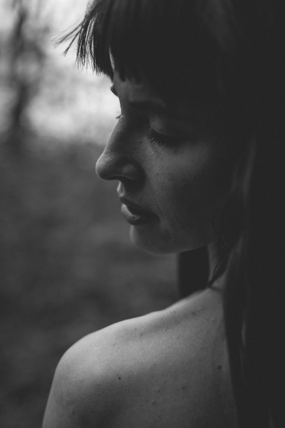 Black and white profile portrait of a person with bangs, captured in dramatic side lighting against blurred background.