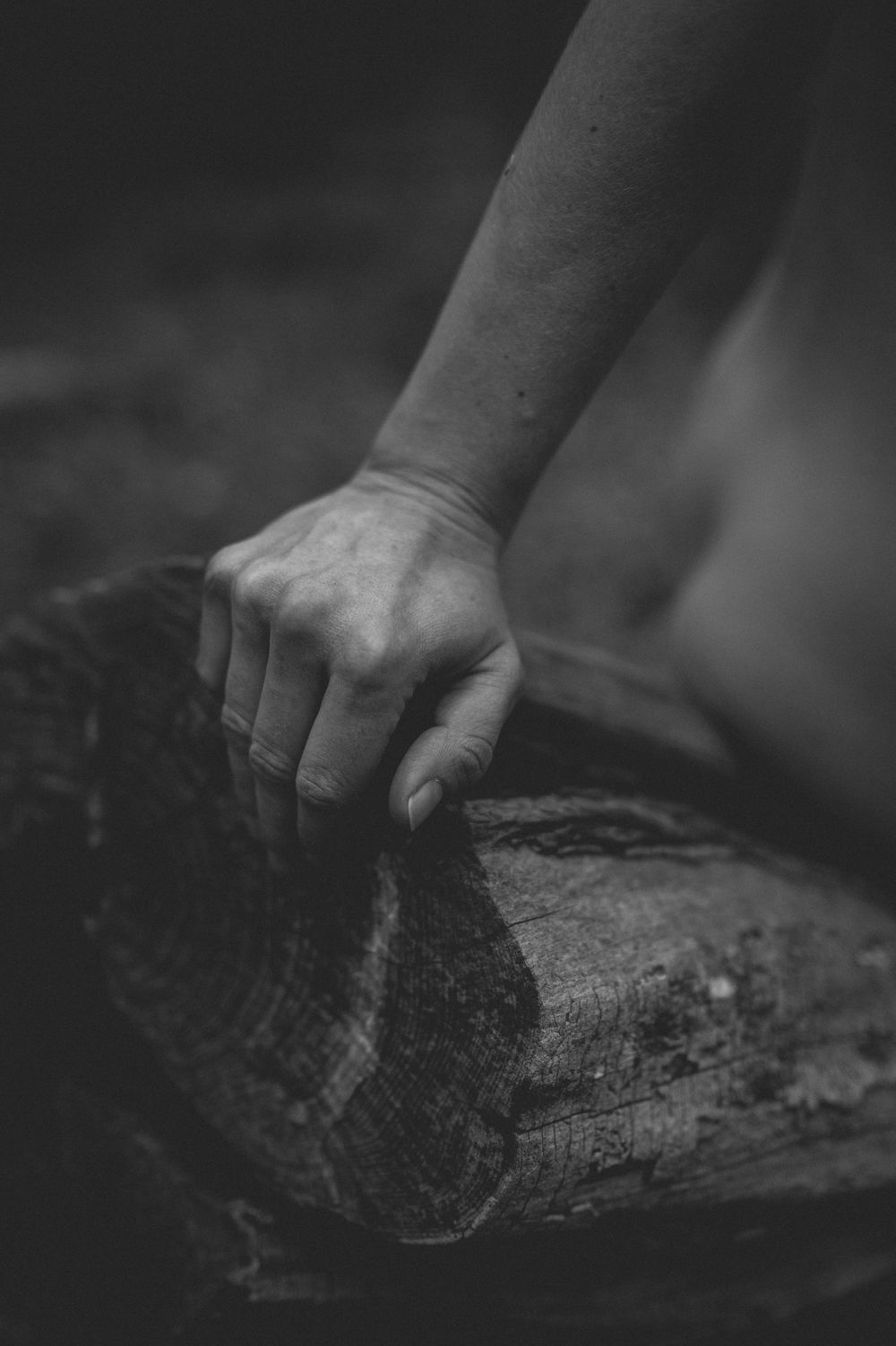 A weathered hand grips a rough wooden log in dramatic black and white photography.