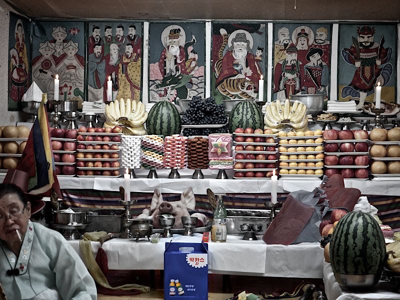 A close-up photo of an old Korean shamanic ritual table arranged with traditional offerings
