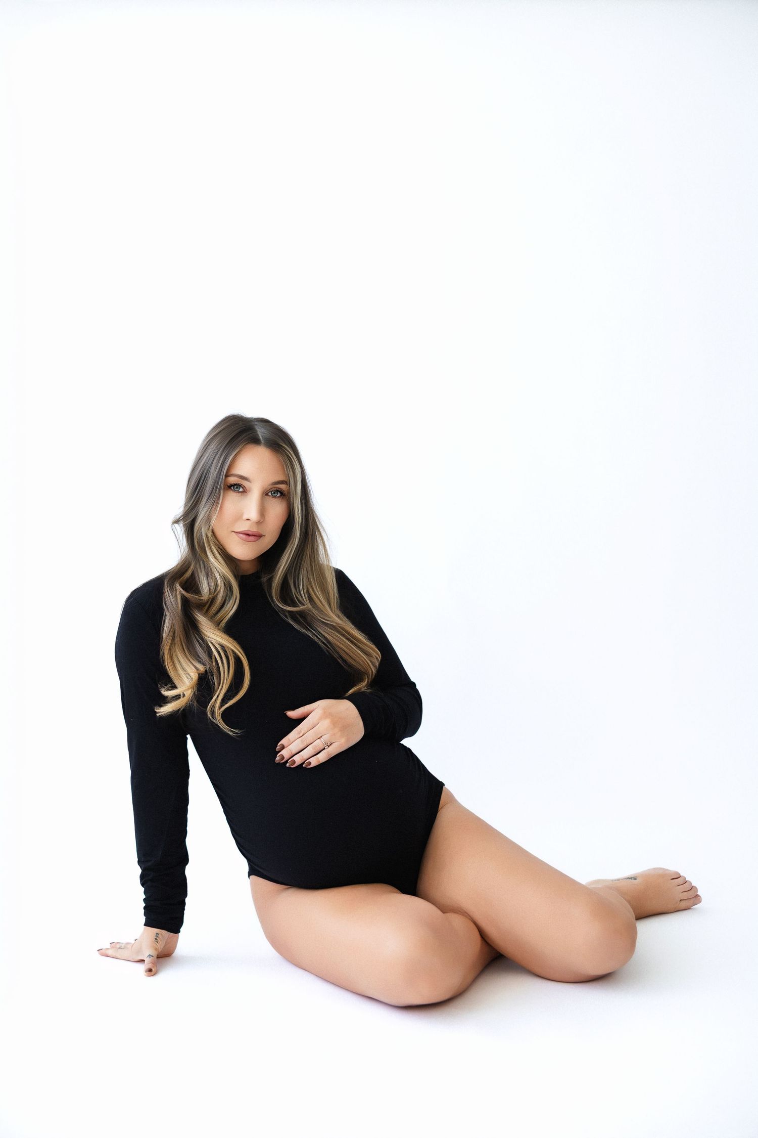 Artistic maternity photo of woman in black bodysuit posing on white background.