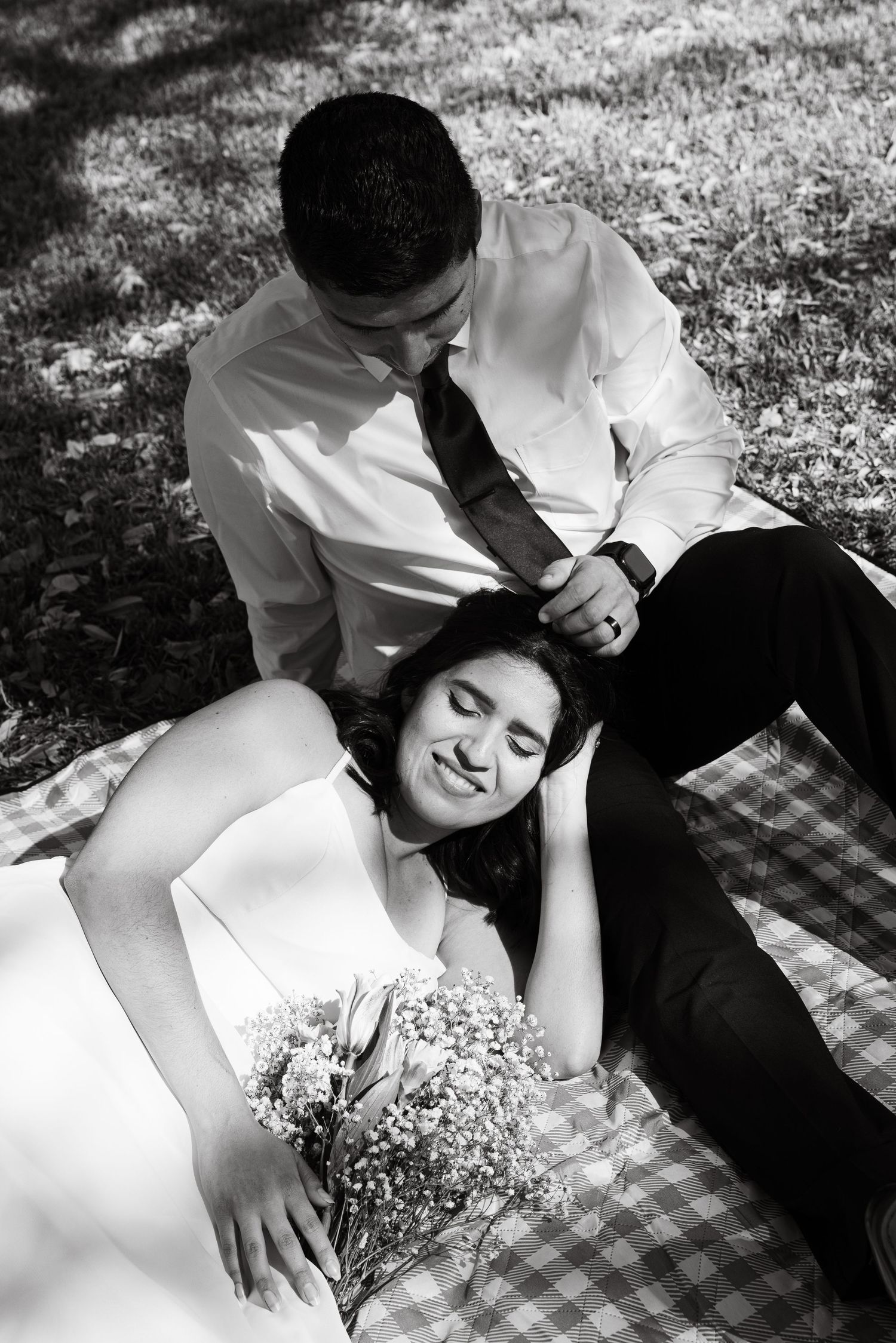 Couple in formal wear relaxes on picnic blanket in black and white photography.