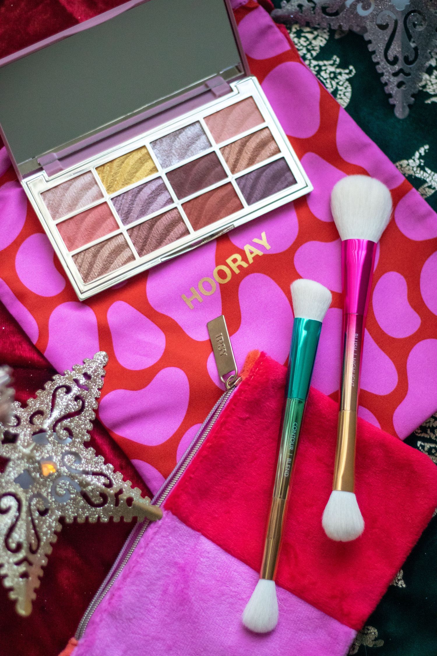 Makeup palette and brushes on vibrant pink background with decorative snowflakes.
